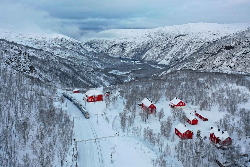 A snowy mountain landscape with red houses and a train track. 1