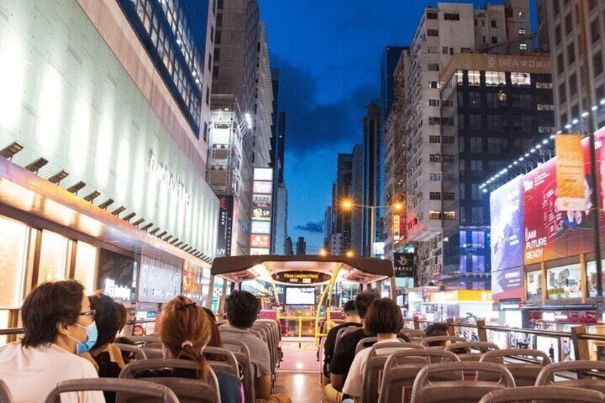 A nighttime cityscape with a bus in the foreground and illuminated billboards in the background. 4