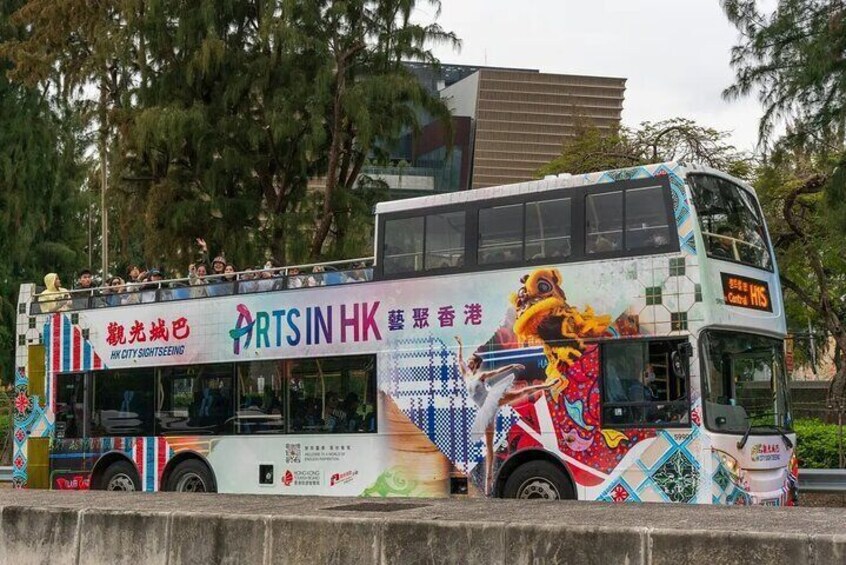 A double-decker bus with colorful artwork and advertisements, parked on a street with trees and buildings in the background. 2
