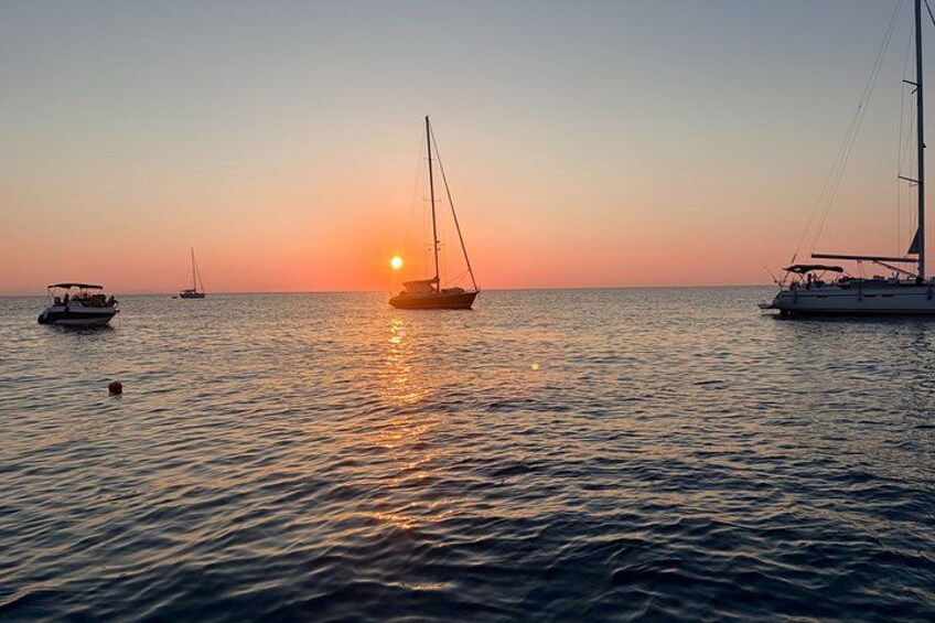 A sunset over calm waters with sailboats and a small motorboat. 4