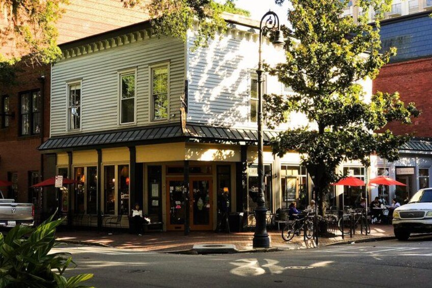 A street with a building that has a green facade and a black awning, a tree, and a bicycle parked in front. 2