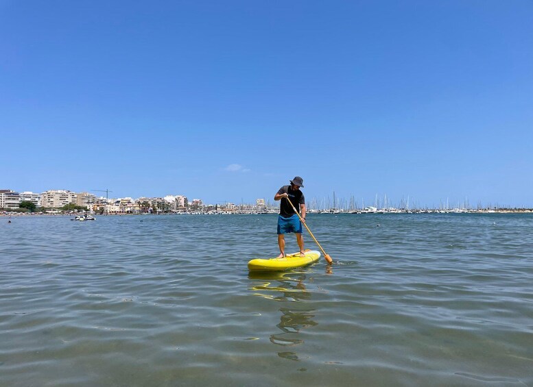 A person paddleboarding on calm waters with a marina and buildings in the background. 4