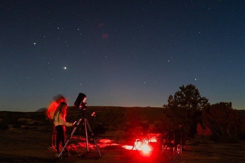 A person using a telescope in a desert landscape at night. 2
