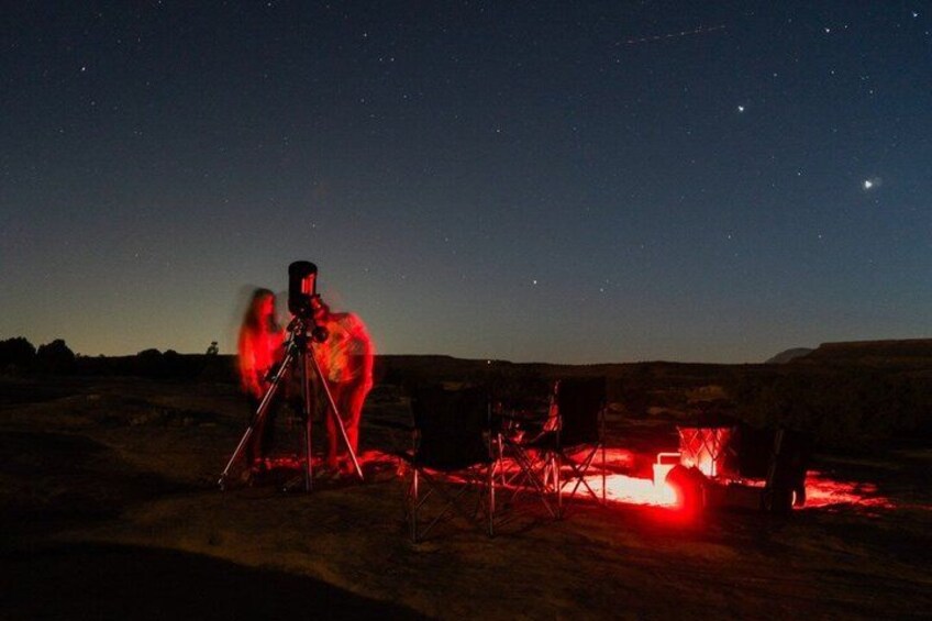 A night scene with a telescope on a tripod, a red light, and a starry sky. 4