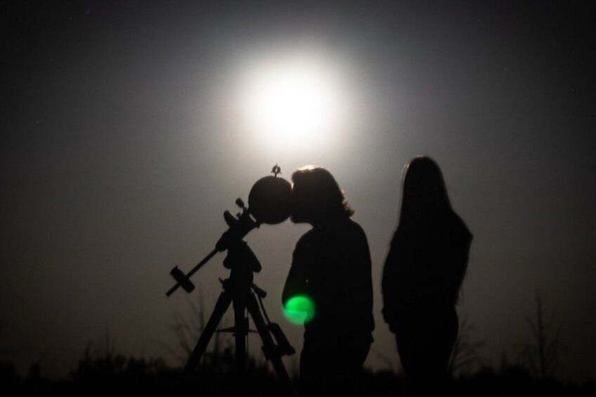 A person using a telescope with a bright light source in the background. 5