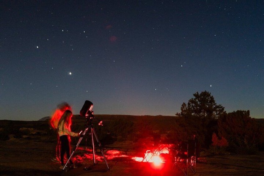 A person with a telescope in a desert landscape at night. 1