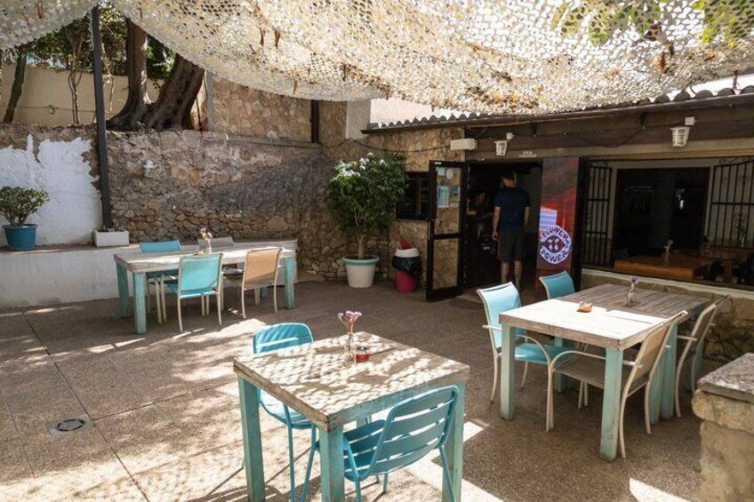 An outdoor café with tables and chairs, a stone wall, and a potted plant. 5