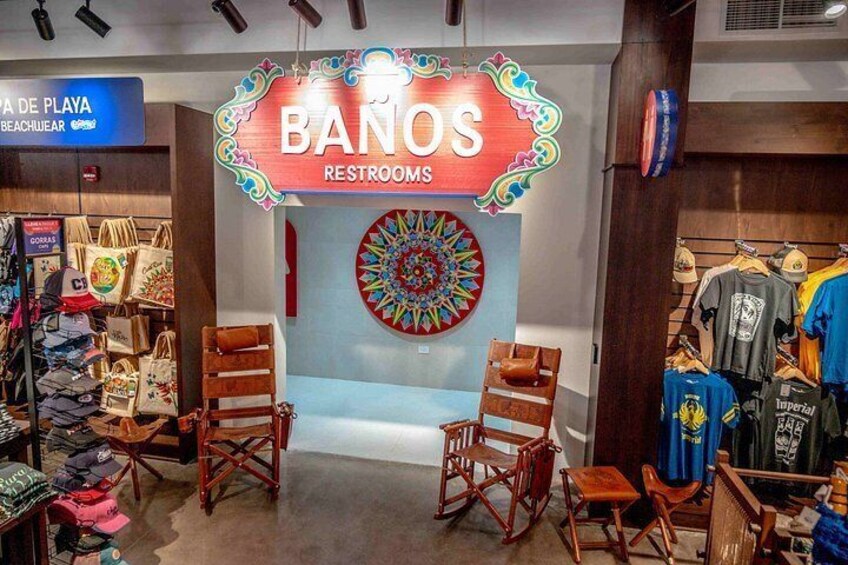 A store named 'BANOS RESTROOMS' with a colorful sign, wooden chairs, and a wall decoration. 5