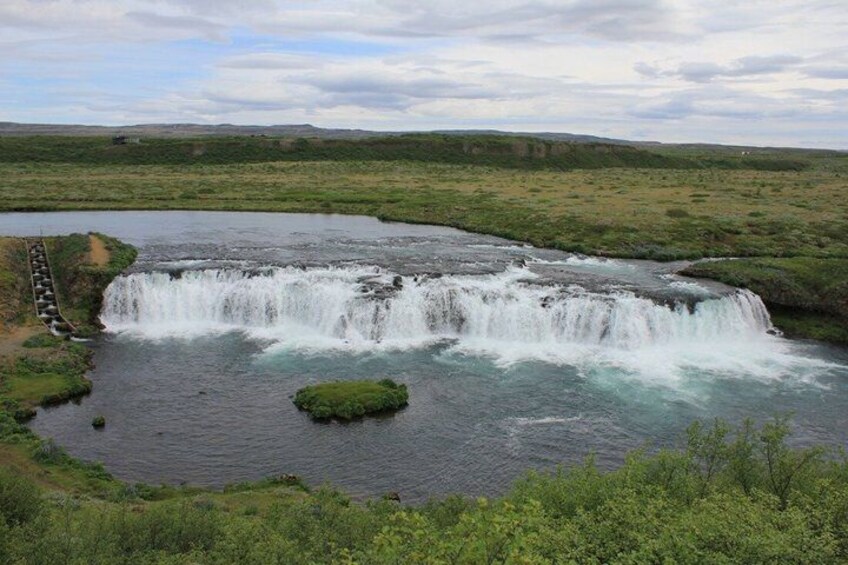 A waterfall cascading over a rocky ledge into a river, surrounded by a flat, grassy landscape. 3