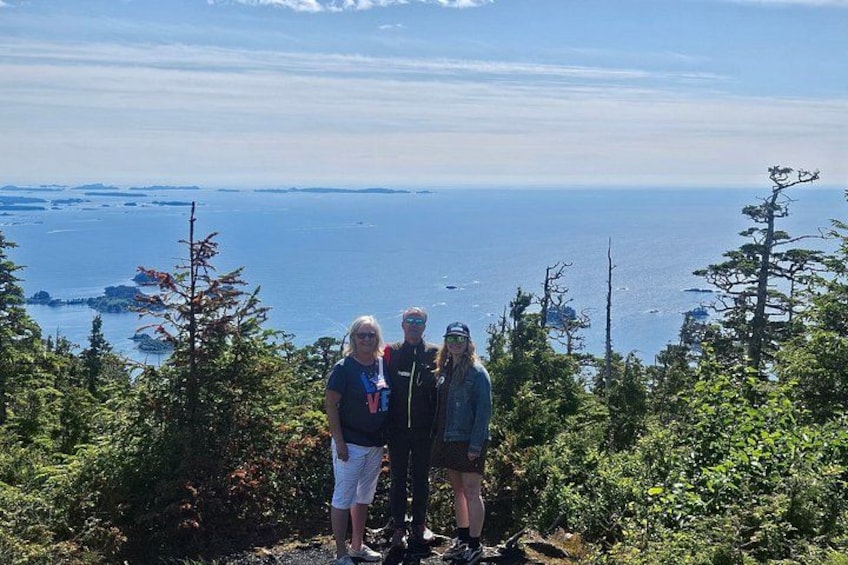 A group of people standing on a mountain overlooking a body of water with trees and a clear sky. 2