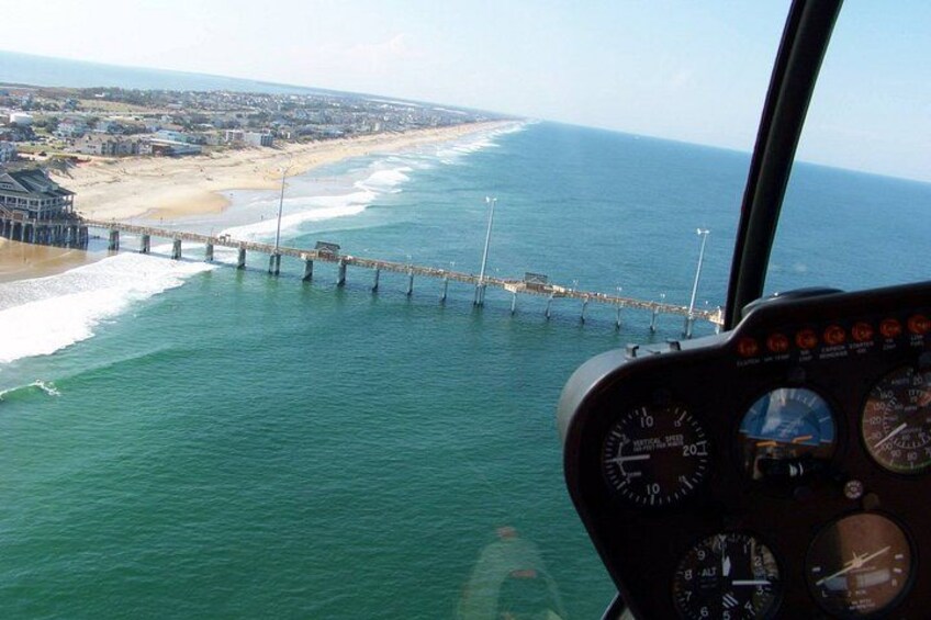 A coastal view with a pier extending into the ocean, a beach, and a clear sky. 1