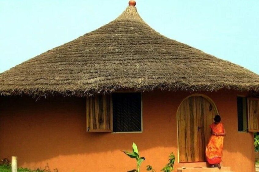 A thatched-roof hut with a single door and window, surrounded by greenery. 3