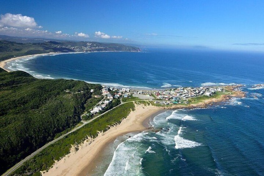 A coastal landscape with a beach, ocean waves, and a town. 1