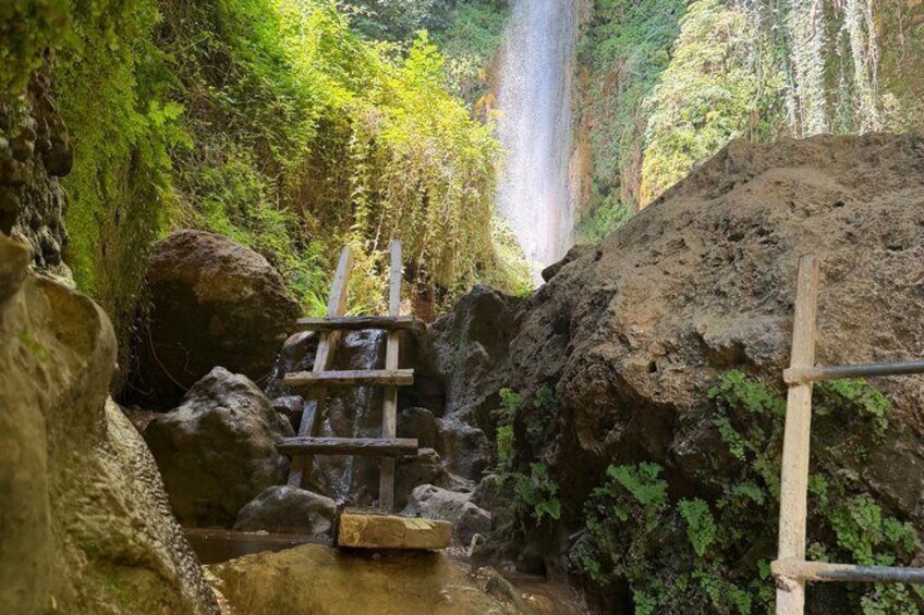 A natural waterfall, a wooden bridge, and a rocky terrain. 2