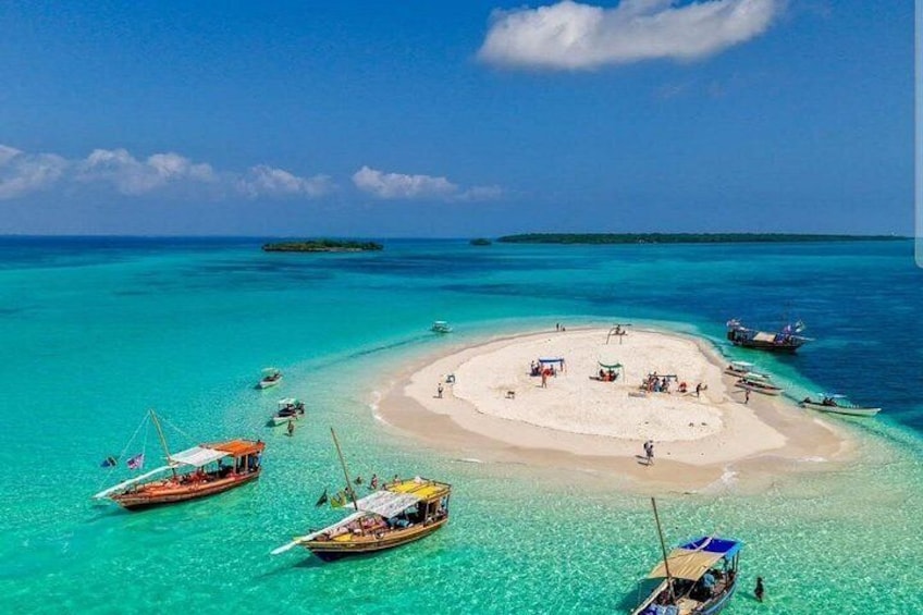 A tropical island with clear turquoise waters, a sandy beach, and several boats anchored around the island. 1
