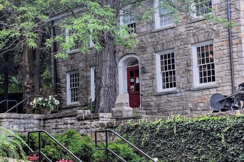 A stone building with a red door, surrounded by trees and a hedge. 3