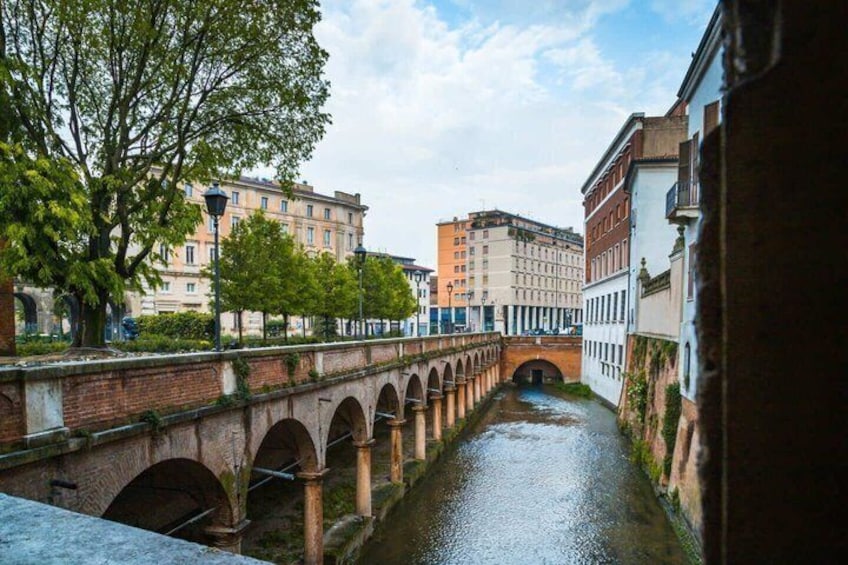 A canal with a brick bridge, buildings, and trees. 3