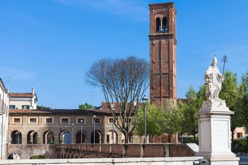 A historic building with a clock tower, a statue, and a bridge. 4