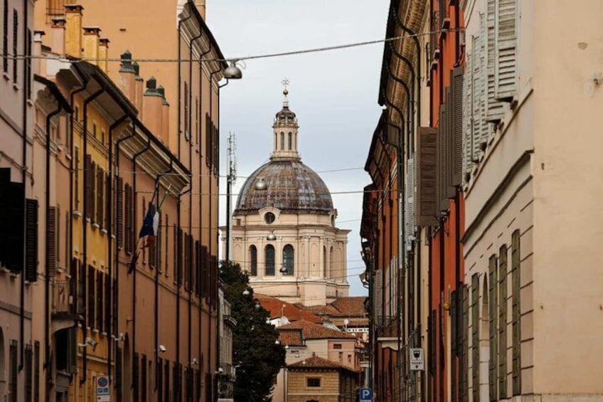 A narrow street with historic buildings, a prominent dome, and a flag. 2