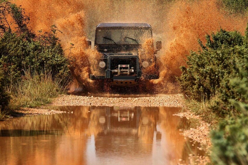 A vehicle driving through a puddle, kicking up water and mud. 4