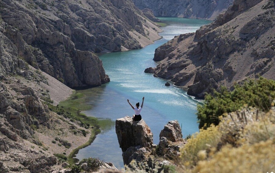 A person standing on a rock with arms raised, overlooking a river in a canyon. 1