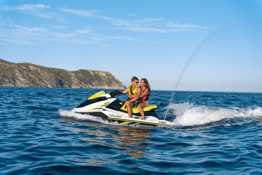 A person jet-skiing on a Yamaha jet ski with another individual on board, with a mountainous coastline in the background. 3