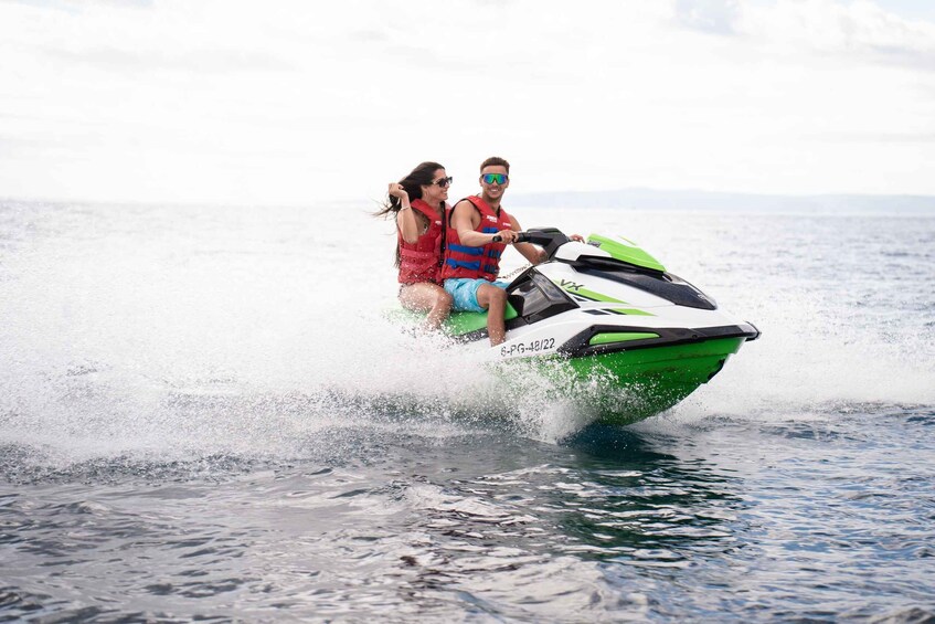 Two people on a green and white jet ski moving through water. 1
