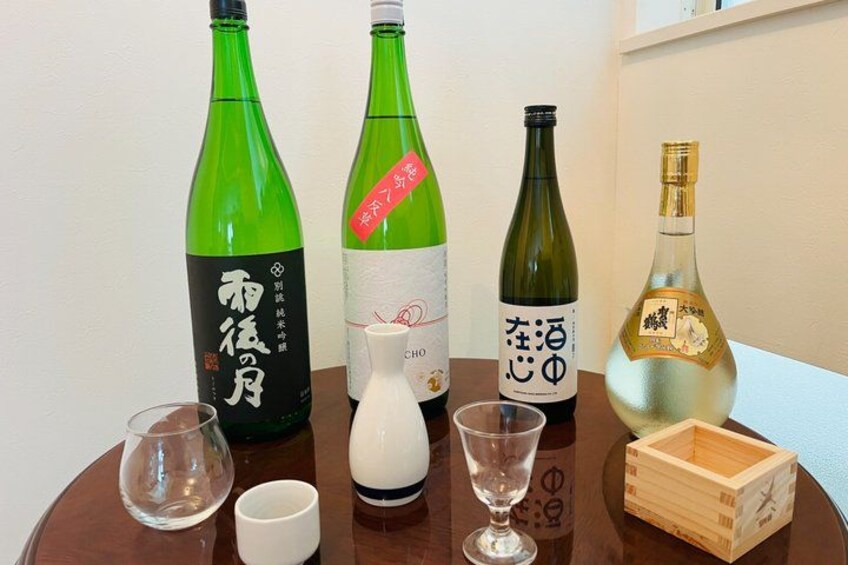 Cuatro botellas de sake japonés con copas y una jarra pequeña sobre una mesa de madera. 3