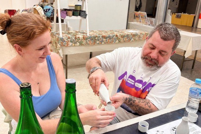 Dos personas sentadas a una mesa con botellas verdes y una blanca. 2