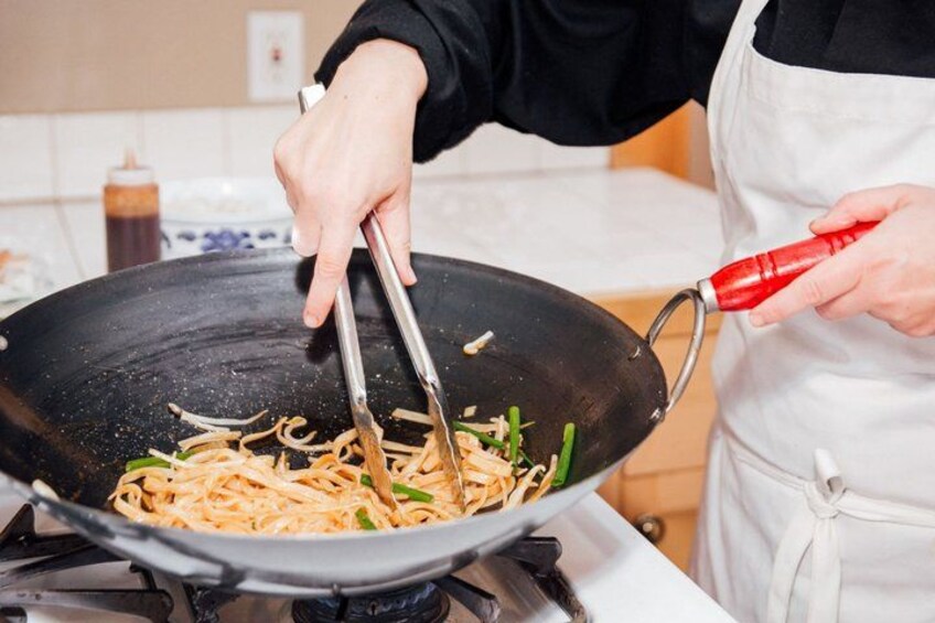 A person cooking noodles in a wok on a stove. 3