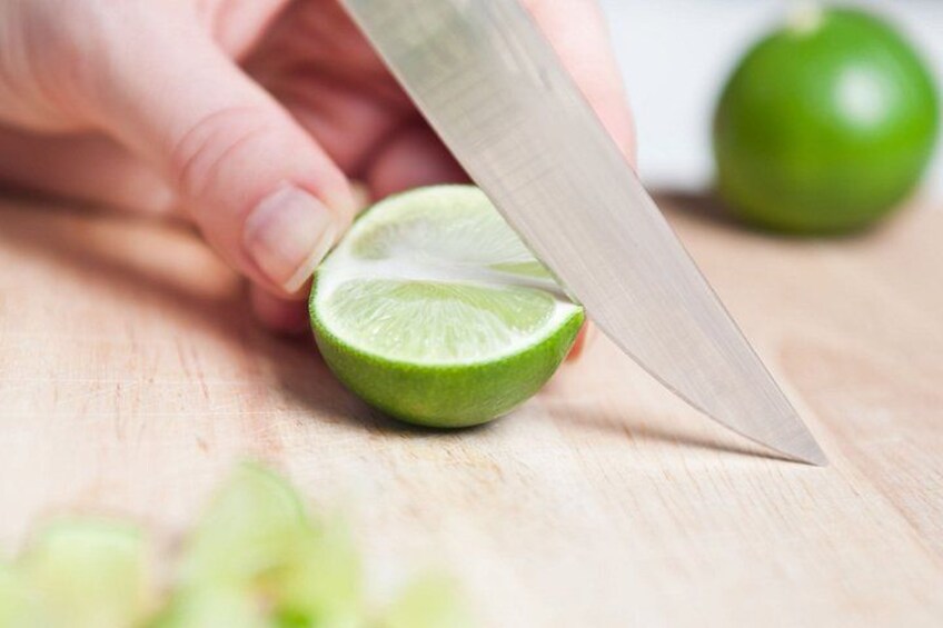 A hand holding a knife cutting a lime on a wooden surface. 2