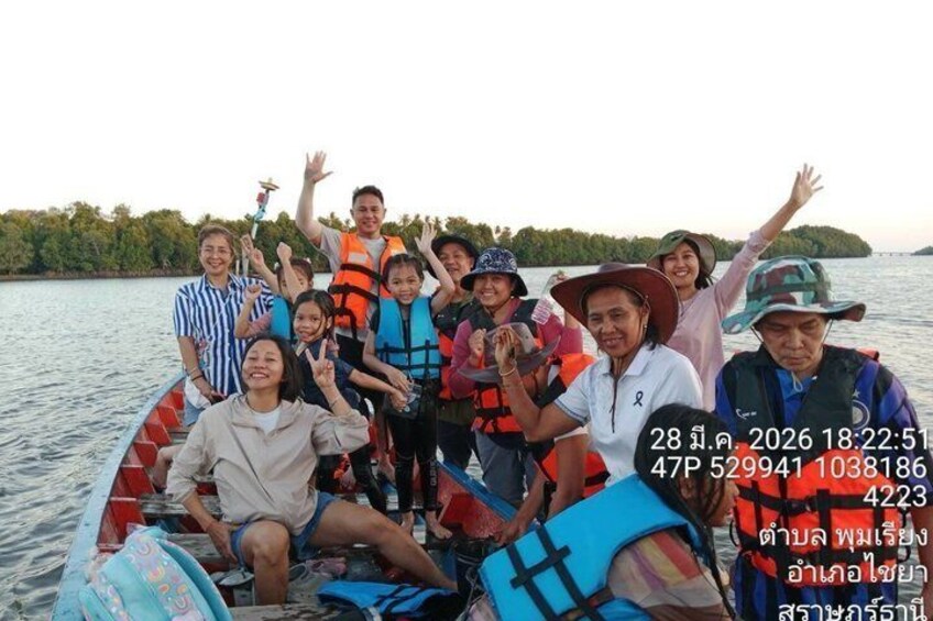 A group of people on a boat with life jackets, a calm body of water, and trees in the background. 3
