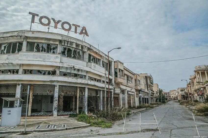 A multi-story building with a 'TOYOTA' sign, boarded-up windows, and a street with a few pedestrians. 4