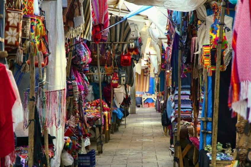 A narrow market street with colorful textiles and fabrics displayed on racks. 2