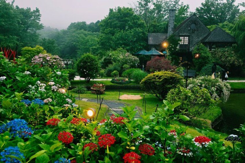 A lush garden with a variety of colorful flowers, a well-maintained lawn, and a house with a porch. 5