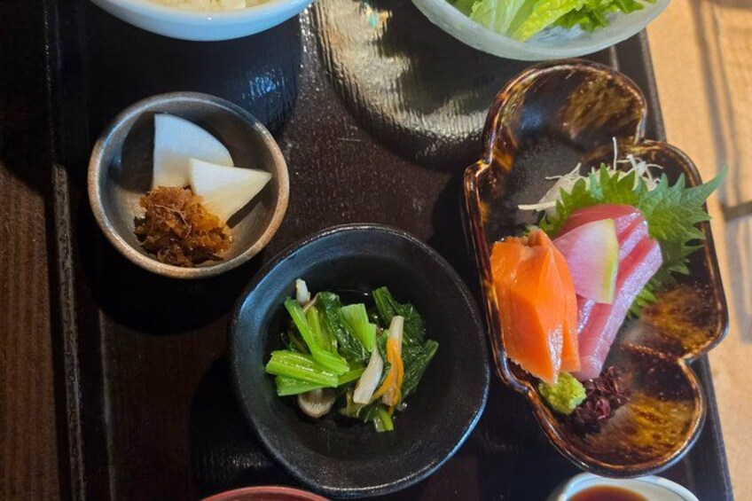 A tray with various food items including a bowl of salad, a dish with salmon and vegetables, and a small bowl of sauce. 3
