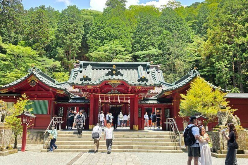 A traditional Japanese temple with a red gate, visitors, and lush greenery in the background. 1