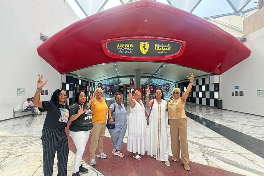 A group of people posing in front of a Ferrari exhibit with a large red car model. 1