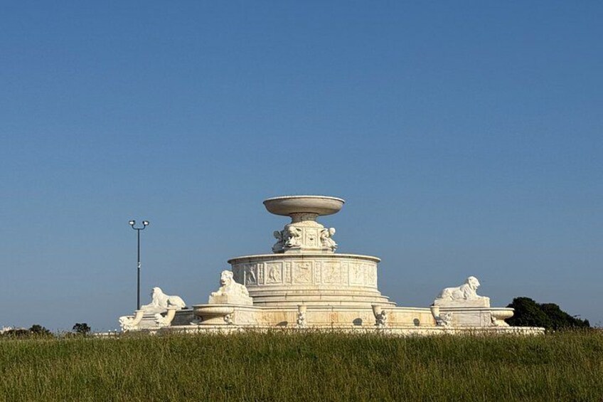 A large, ornate fountain with multiple tiers and sculptures, set in a grassy field under a clear sky. 4