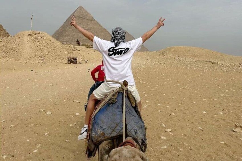 A person on a camel with arms raised, a pyramid in the background, and a desert landscape. 2