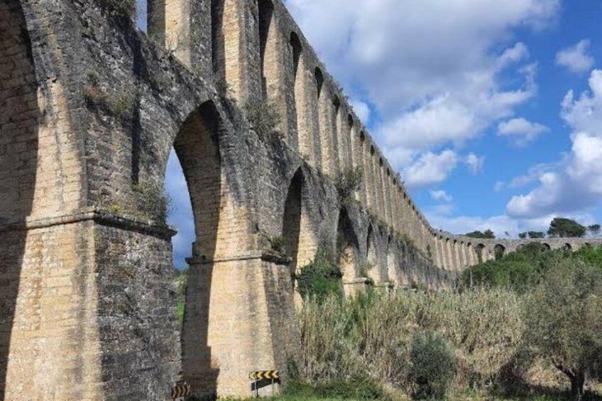 A stone aqueduct with multiple arches, surrounded by vegetation and a clear sky. 3