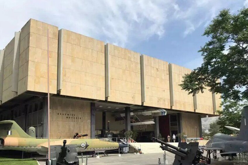 A museum building with a modern design, featuring a large entrance and several aircraft on display in front. 1