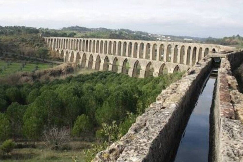 A long aqueduct with arches, a narrow water channel, and a hilly landscape with greenery. 4
