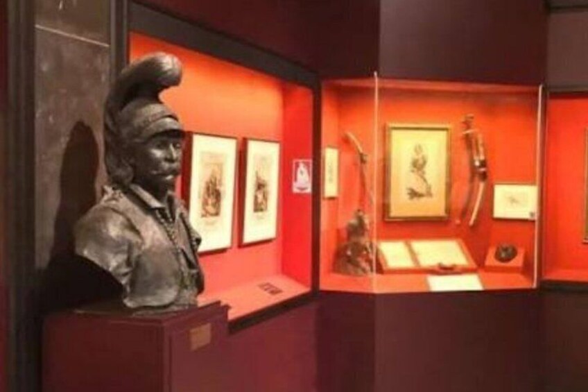 A museum exhibit with a bust sculpture, framed artwork, and historical artifacts. 2