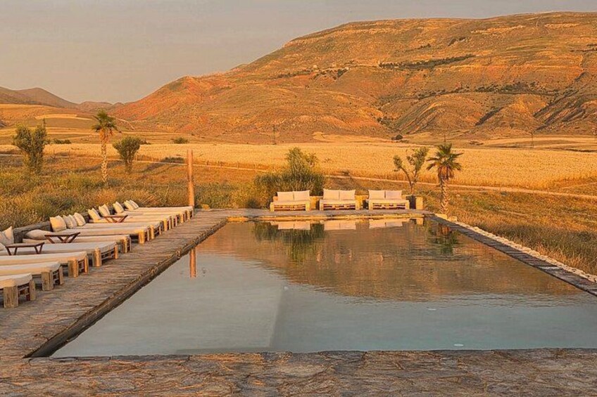 A swimming pool with lounge chairs, palm trees, and a desert landscape with hills in the background. 4