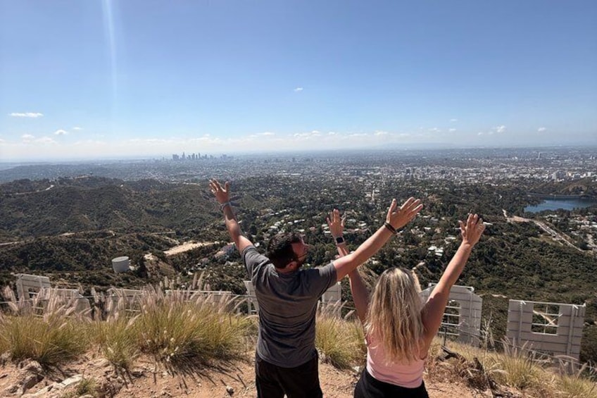 Two people standing on a hill with their arms raised, overlooking a cityscape. 1