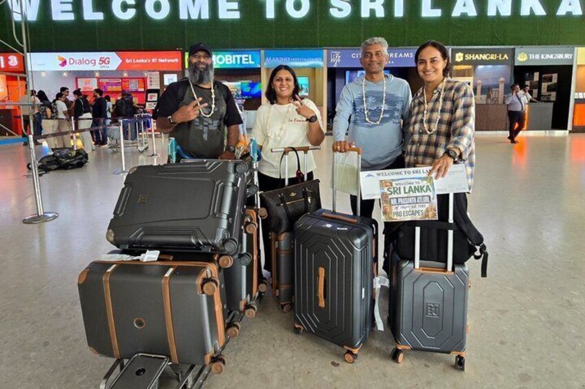 A group of people with luggage at an airport, a sign reading 'Welcome to Sri Lanka', and various airline and network signs in the background. 2