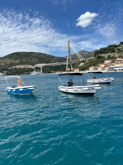 A coastal scene with several boats on calm blue waters, a bridge in the background, and a hilly landscape with buildings. 5