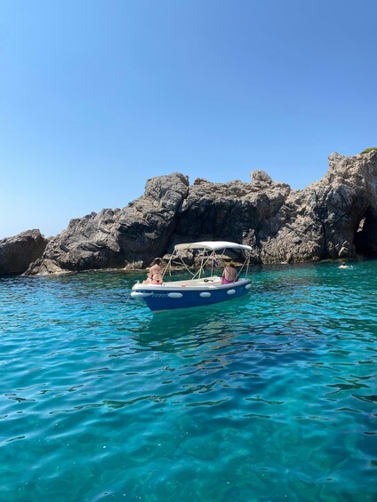 A boat with two people on a clear blue sea, rocky cliffs in the background. 4