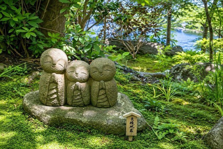 A stone sculpture of three figures in a forested area with a pond in the background. 4